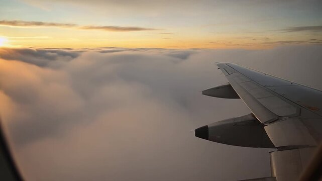 Airplane wing flying above clouds during sunrise or sunset, aerial view