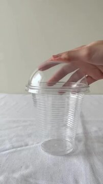 Hand opening plastic cup on a white textured tablecloth against a beige wall