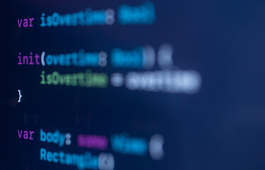 Closeup of programming code on a dark computer screen, with colorful syntax highlighting as a developer edits Swift-style variables and functions for a mobile app

