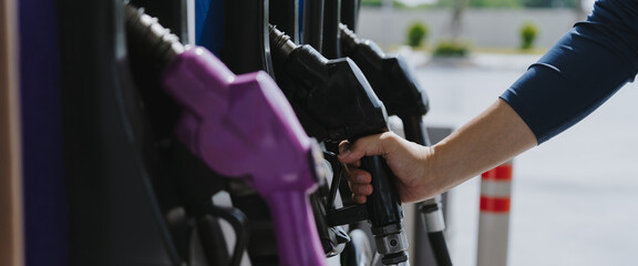 A close-up image of a gas station attendant's hand holding a fuel dispenser.	
