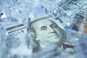 Close up frozen one hundred US dollar bill banknote with ice cubes. Global financial crisis, frozen UD dollar value, world currency market, US economy, investment, tariffs war and so on concept.