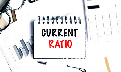 Current ratio concept on notepad with charts, calculator, pen and glasses on white desk