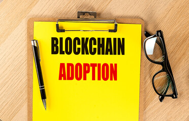 Blockchain adoption concept on yellow clipboard with pen and eyeglasses on wooden desk