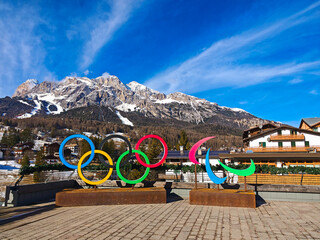 Fototapeta premium CORTINA D'AMPEZZO, ITALY - JANUARY 22, 2025: Vibrant Olympic Rings installation in Cortina d'Ampezzo with the snow-covered Italian Dolomites mountains in the background under a blue sky