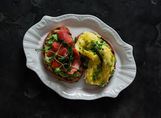 Breakfast, brunch, snack sandwiches with avocado, omelette and lightly salted salmon on a dark background, top view