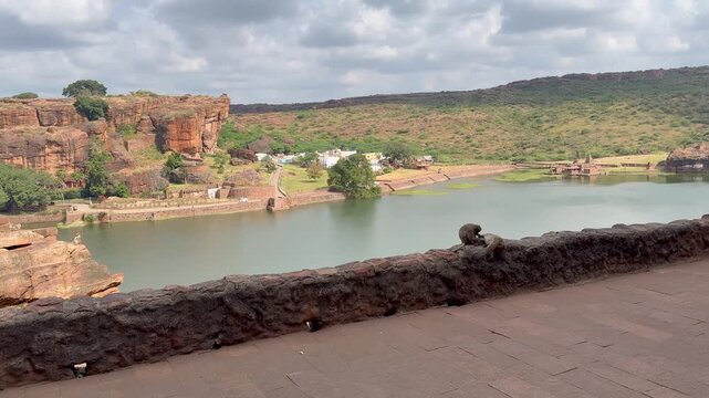 Panoramic view of the Bhoothnath Temple, the vast Agastya Lake, dramatic red sandstone mountain ranges, lush green hills, and monkeys resting along the rocky landscape