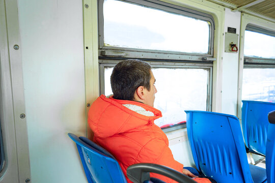 Male passenger in a jacket sitting in an empty train carriage. Represents an anti-goal travel mindset, a process-oriented journey, meandering without an itinerary, and sustainable wandering practices.