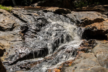 A small, serene waterfall cascades over dark, glistening rocks in a continuous, gentle flow, capturing the pure, raw beauty of nature in motion in Brazil. © AlfRibeiro