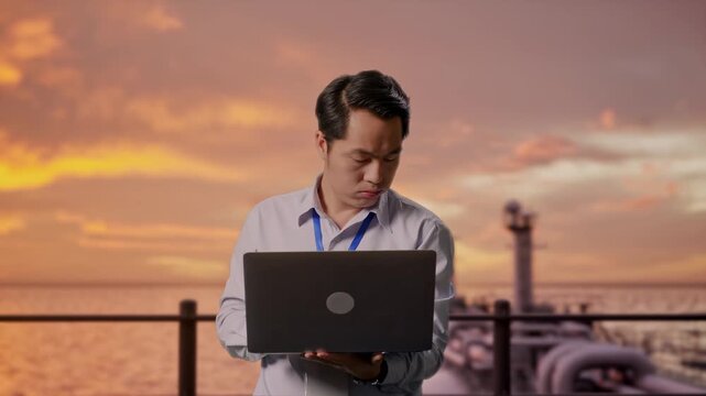 Asian Male Professional Worker Standing With His Laptop at the Deck of a Large LNG Tanker or Offshore Energy Platform at Sunset, He Is Nodding His Head With Dissapionted