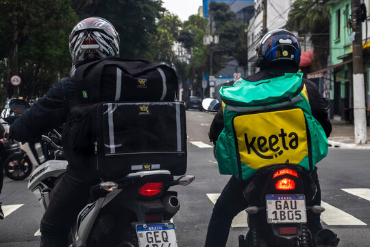 Sao Paulo, Brazil, December 19, 2025. Two motorcycle couriers from a delivery app waiting in traffic. A view from behind showing the daily life of gig economy workers in a Brazilian city,