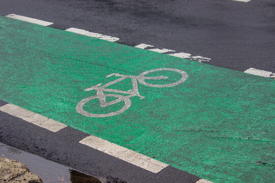 Green colored bike lane on asphalt road with white bicycle symbol, made of thermoplastic paint for cyclist safety in Kembangan, West Jakarta.