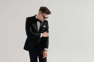 Stylish man in tuxedo looking down and fixing sleeve