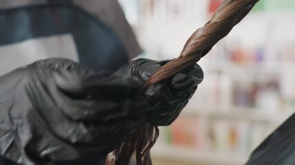 saturated brown strand receiving professional hair treatment inside salon, closeup of styled brown hair being treated by professional stylist with gloves in vibrant salon environment