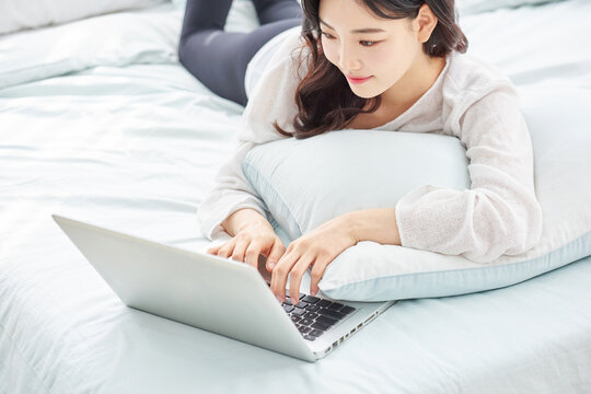 Young woman using laptop while lying on bed