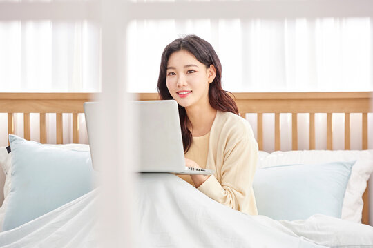 Young woman working on laptop in cozy bedroom.