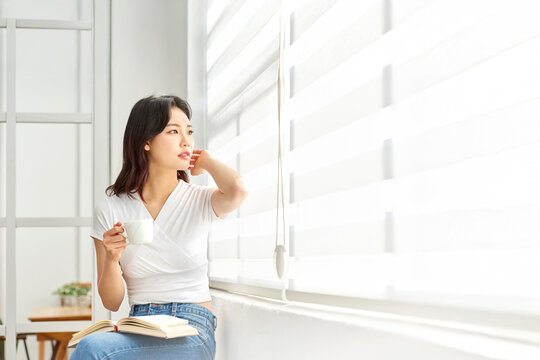 Young woman relaxing by window with book and teacup