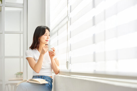Young woman relaxing by window with book and teacup