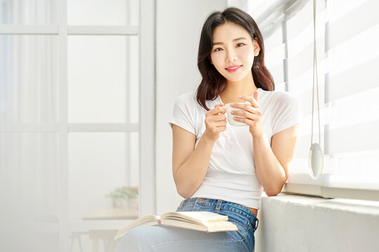 Young woman relaxing by window with book and teacup
