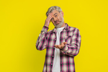 Caucasian middle-aged mature man on yellow background placing hand on forehead, heavy sigh indicating weariness. Disappointment, repeated failures creating visible irritation, comedic facepalm style