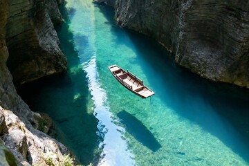 A wooden boat floats on clear turquoise water in a narrow canyon with steep rock walls.