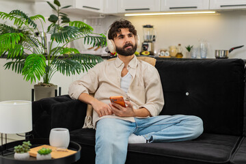 Indian man at home uses orange smartphone plays music with wireless headphones moves slowly in...