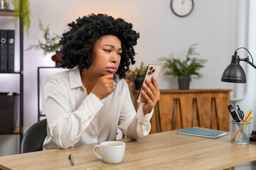 African American businesswoman at home office reads smartphone stunned by news and game defeat...