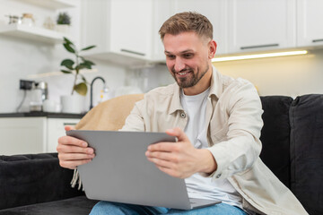 Young man at home works as freelancer checks laptop sees project approval and celebrates with joy....