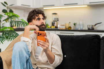 Indian man at home works on smartphone typing messages for freelance clients in chat app busy at work. Arabian guy checks orange mobile phone writes reply to customer message feels busy concentrated.