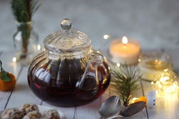 A transparent teapot with black tea on a wooden table. Sesame seed candies lie nearby.