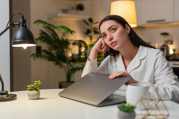 Young woman at night home shuts laptop after work feels burnout wants pause takes breath. Caucasian girl on sofa at table at evening looks tired says enough rubs temples needs break rests eyes closed.