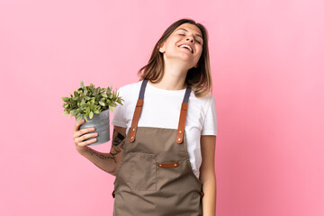Gardener woman holding a plant isolated on pink background laughing