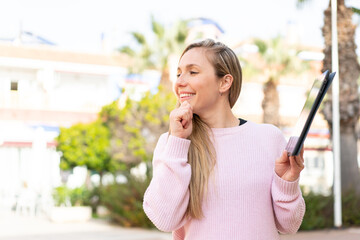 Fototapeta premium Young blonde woman holding a tablet at outdoors thinking an idea and looking side