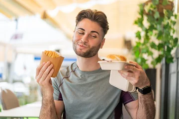 Fotobehang Onderzeeër Young handsome man holding a burger and fried chips  © luismolinero
