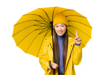 Young Asian woman with rainproof coat and umbrella over isolated chroma key background showing and lifting a finger in sign of the best