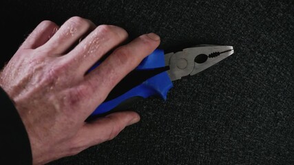 Hand grabbing blue pliers and opening and closing tool on black background
