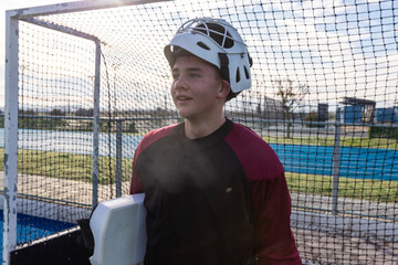 Teenage boy standing in front of goal in caged helmet and blocker pad on sports field