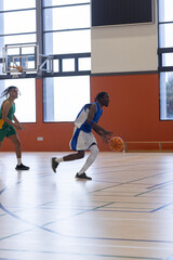 Obraz premium Diverse male basketball players in jersey dribbling and defending at gym court with hoop bench