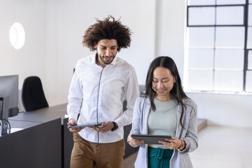 Diverse coworkers in business attire walking and consulting tablets in office