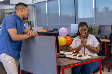 Obraz premium Diverse coworkers celebrating birthday in open-plan office with cupcakes, balloons, copy space