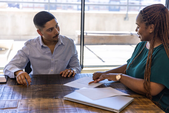 Diverse coworkers in business attire reviewing documents at conference table with laptop - Powered by Adobe