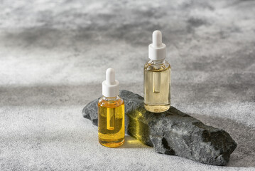 Set of dropper bottles with cosmetic serum on a stone podium, selective focus.
