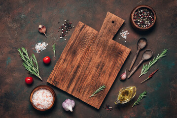 Wooden cutting board and various cooking ingredients on a dark grunge background, culinary backdrop. Top view, flat lay, copy space.