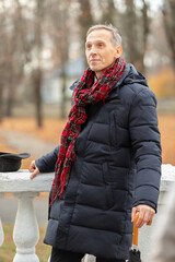 Elderly man enjoying a cool autumn day in a park while wearing a warm coat and scarf with a cane