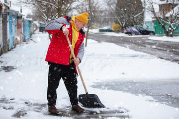Man shovels snow in a residential area wearing warm clothes during a snowstorm in winter