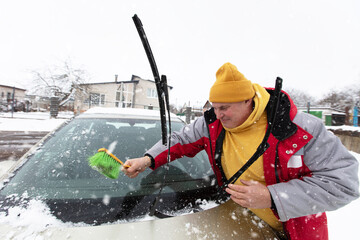 Man removes snow from car windshield in winter weather on a snowy day in a residential area