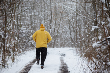 Jogging through a snowy forest path in winter with a yellow jacket and snowflakes falling