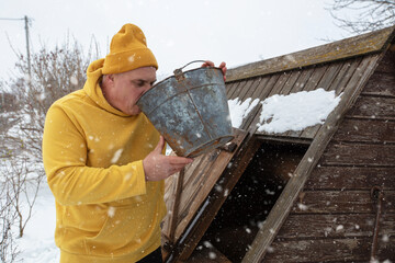 Man collects water from a bucket in the snowy countryside during winter