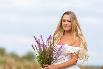 Woman holding bouquet of purple flowers in a field during a cloudy day