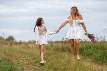 Mother and daughter enjoy a sunny day in a flower field while holding hands and sharing smiles