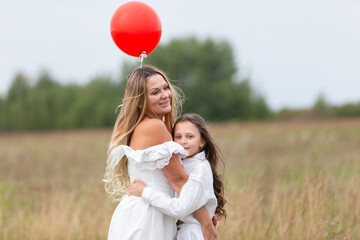 Mother and daughter enjoy a playful moment in a green field with a red balloon on a cloudy day